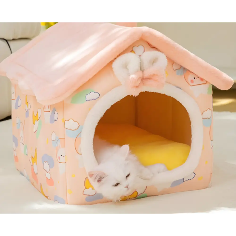 Pink house-shaped cat bed with cloud patterns and a white kitten sleeping inside.