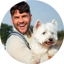 A happy person holding a fluffy white West Highland Terrier dog.